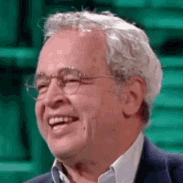 a close up of a man wearing glasses and a suit smiling .