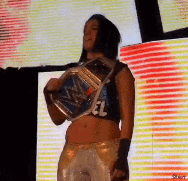 a woman in a crop top with el on it is holding a wrestling championship belt