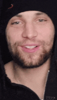 a man with a beard wearing a black beanie and a black jacket is smiling .