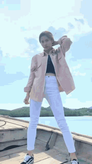 a woman wearing a pink jacket and white pants stands on a boat