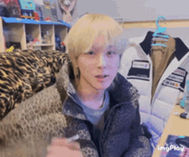 a man with blonde hair is sitting on a couch with a leopard print jacket on