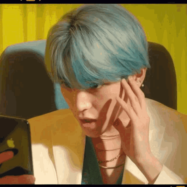 a young man with blue hair is looking at his phone .
