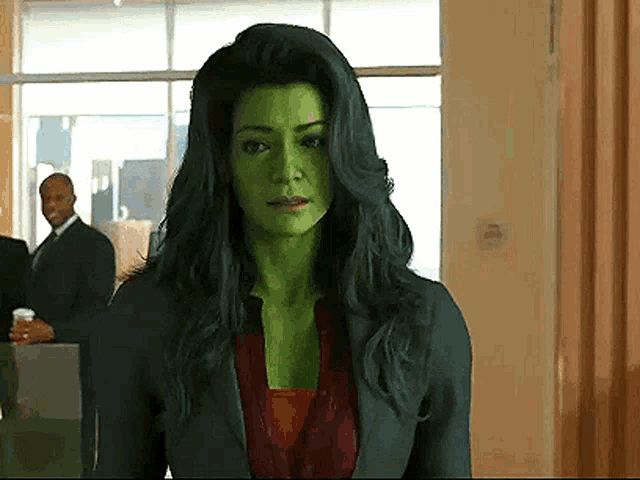 a woman with green hair and green face is standing in a hallway