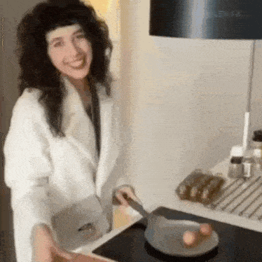 a woman in a white coat is cooking eggs in a pan on a stove .