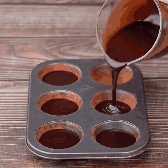 a cup of chocolate is being poured into a muffin tin