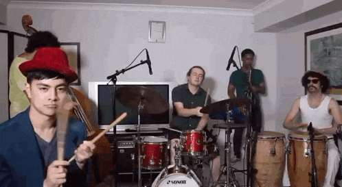 a man in a red hat is playing drums in a band with other men .