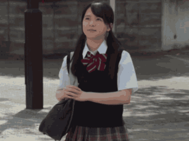 a girl in a school uniform holds a bag