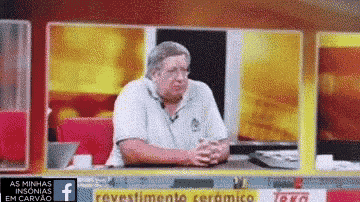 a man is sitting at a table with his hands folded in front of a sign that says ' revestimento ceramico '
