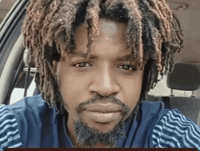 a man with dreadlocks and a beard is sitting in a car looking at the camera .