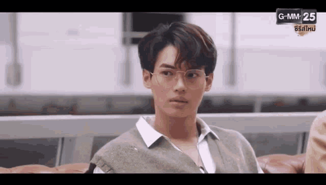 a young man wearing glasses is sitting on a couch and looking at the camera .