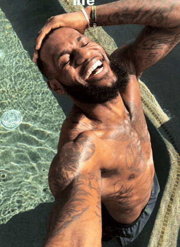 a shirtless man is taking a selfie in a pool with the word life on the bottom right