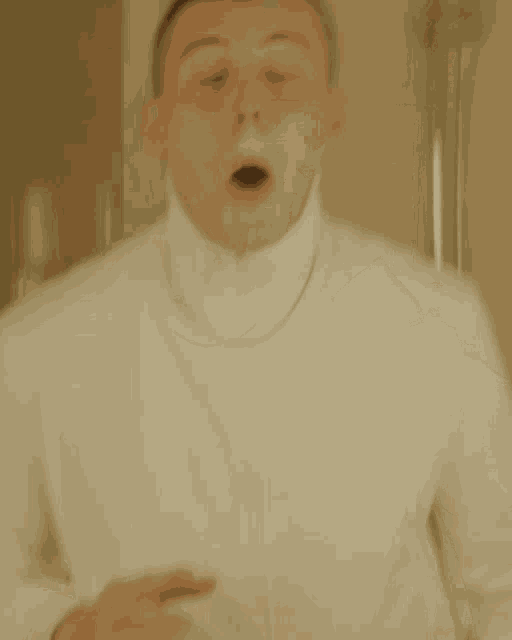 a man wearing a white turtleneck covering his face