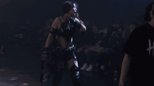 a woman in a black top and gloves is dancing in front of a crowd