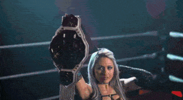 a woman in a wrestling ring is holding a championship belt over her head