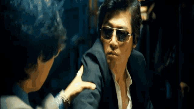 a man in a suit and sunglasses is being held by another man in a white shirt .
