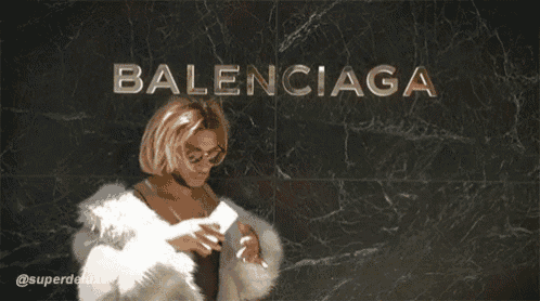 a woman in a fur coat taking a selfie in front of a balenciaga sign