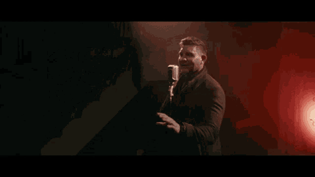 a man is singing into a microphone in a dark room with red lights .