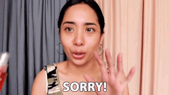 a woman is making a sorry gesture with her hands while wearing earrings .