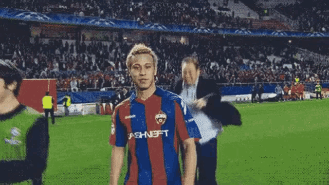 a man in a striped shirt with the word ashneft on it is walking on a soccer field .