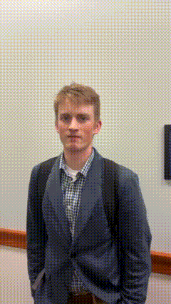 a man in a suit and plaid shirt stands in front of a wall