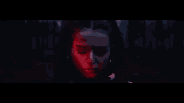 a close up of a woman 's face in the dark with red lights behind her