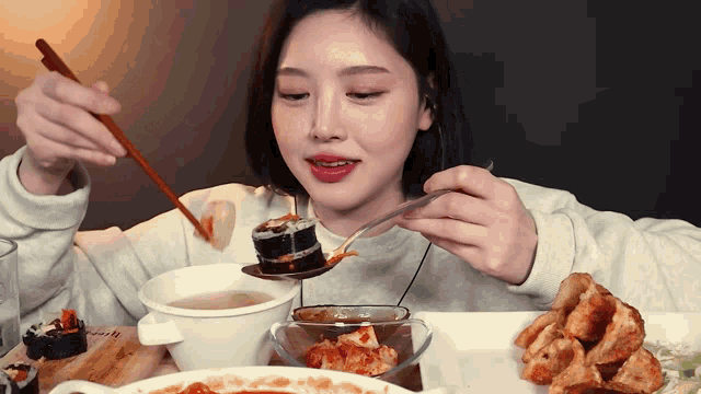 a woman is eating food with chopsticks and a spoon and a bowl of soup