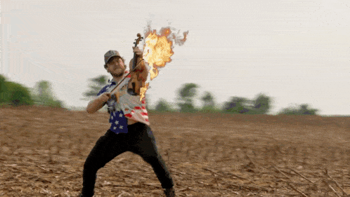 a man in an american flag shirt is playing a violin on fire
