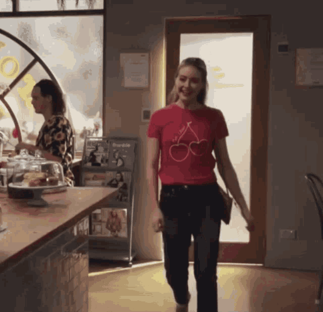 a woman wearing a red t-shirt with cherries on it walks through a restaurant