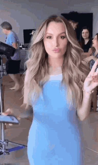 a woman in a blue dress is standing in front of a camera and making a funny face .