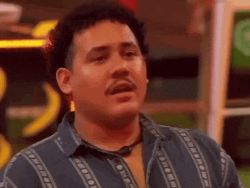 a man with curly hair and a mustache is wearing a blue shirt and a necklace .