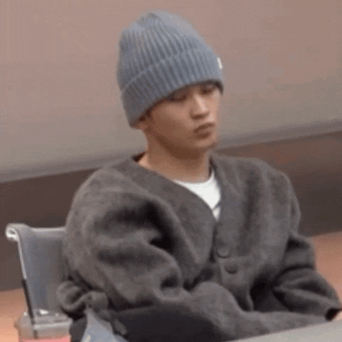 a man wearing a beanie and a sweater is sitting in a chair .