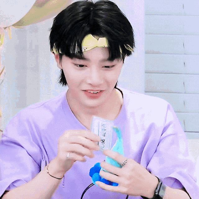 a young man wearing a purple shirt and a headband is holding a stuffed animal and smiling