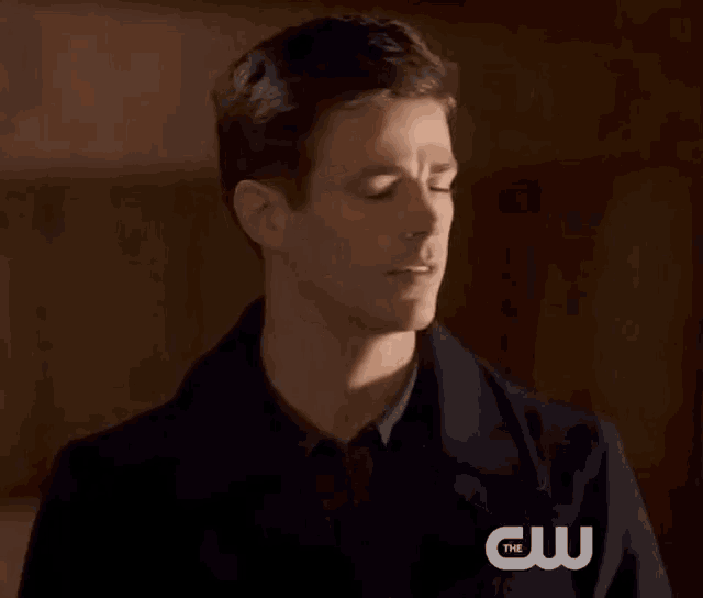 a man with his eyes closed is wearing a jacket with the cw logo