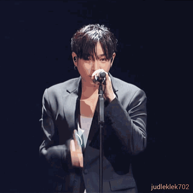 a man in a suit singing into a microphone with judleklek702 written on the bottom right