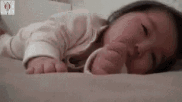 a baby is laying on its stomach on a bed with its eyes closed .
