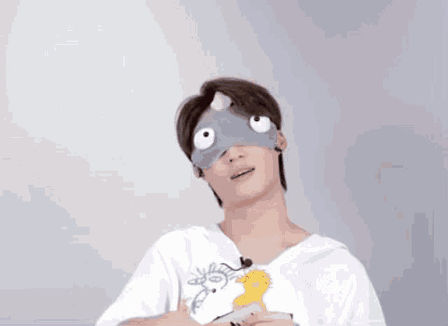 a young man wearing a sleep mask with big eyes and a cat on his head .