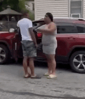 a man and a woman are standing in front of a red suv .