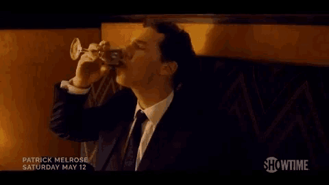 a man in a suit and tie is sitting at a table holding a glass of wine .