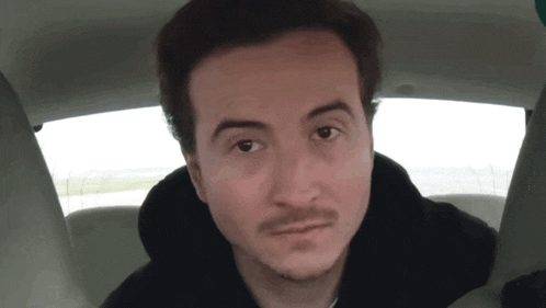 a man with a beard is sitting in a car looking at the camera