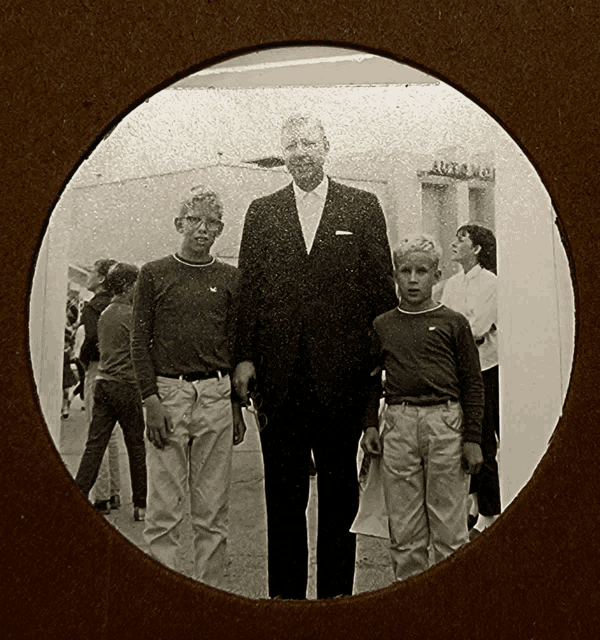 a man in a suit stands next to two young boys in front of a building that says ' arcade ' on it
