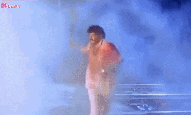 a man in a red shirt and white pants is standing in a foggy room holding a sword .