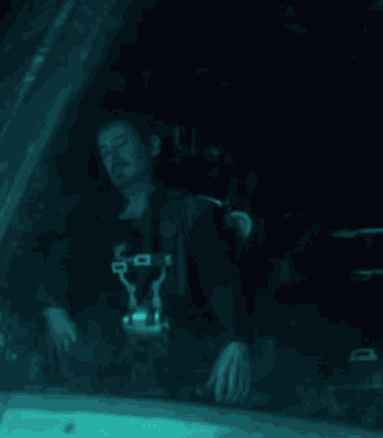 a man wearing a shirt that says ' a ' on it is sitting in a dark room