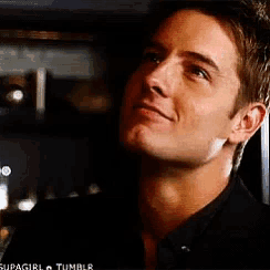a man in a black shirt is smiling and looking up at the sky
