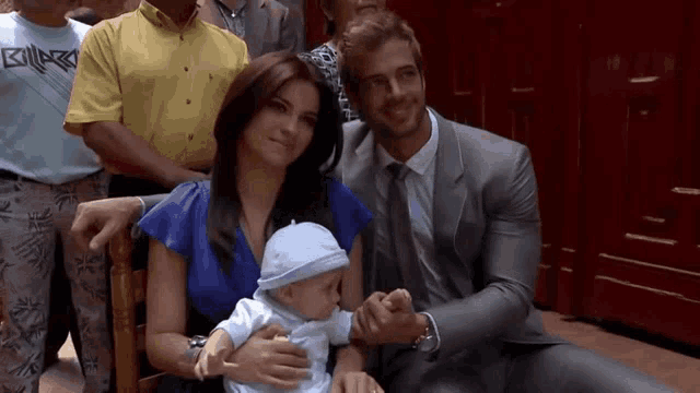 a man in a suit holds a baby while a woman in a blue shirt holds a baby