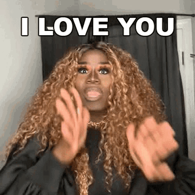 a woman with curly hair is making a funny face and says `` i love you '' with her hands .