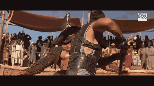 a man in a gladiator costume is fighting another man in front of a crowd that says planet box plus