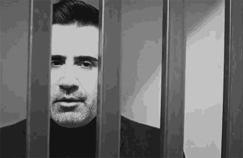 a man is behind bars in a jail cell and looking through the bars .