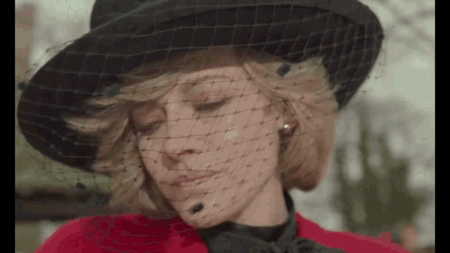 a woman wearing a black hat and veil is looking down .