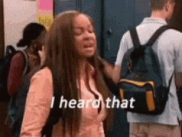 a girl with a backpack is standing in front of a group of people and saying `` i heard that '' .