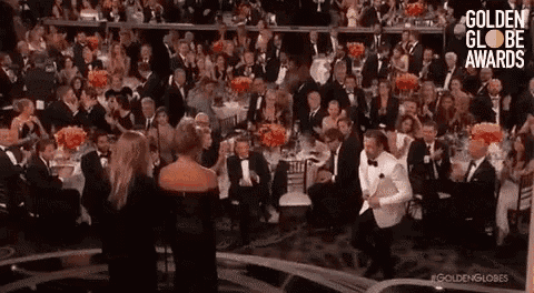 a man in a tuxedo is dancing in front of a crowd of people at a golden globe awards event .